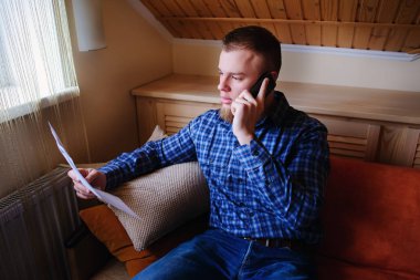 Kağıt basılı tutup evde kanepede otururken cep telefonda konuşurken ciddi olgun adam