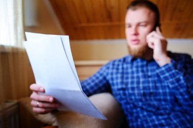 Kağıt basılı tutup evde kanepede otururken cep telefonda konuşurken ciddi olgun adam