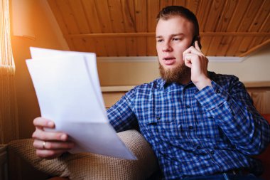 Kağıt basılı tutup evde kanepede otururken cep telefonda konuşurken ciddi olgun adam