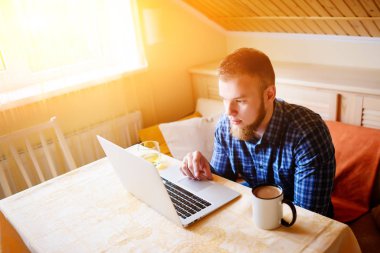 Onun laptop içinde internette sörf rahat genç profesyonel bir yemek odası.