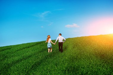 Mutlu aşıklar çayır yeşil çim ve arkasından mavi gökyüzü ile çalışan.