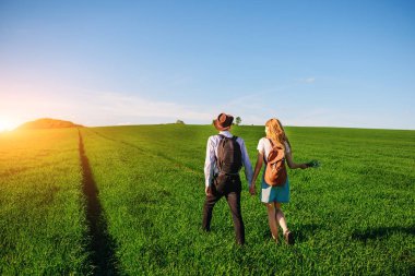 Bir sırt çantası ile bir adam bir şapka ve uzun saçlı bir kadın yol boyunca gidin. Çayır boyunca birkaç yürür.