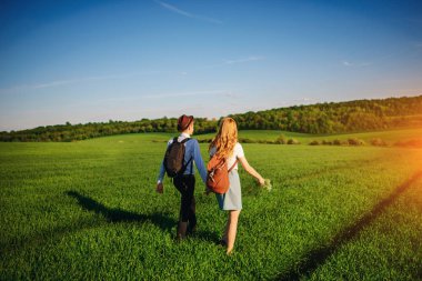 Bir sırt çantası ile bir adam bir şapka ve uzun saçlı bir kadın yol boyunca gidin. Çayır boyunca birkaç yürür.