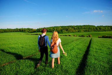 Bir sırt çantası ile bir adam bir şapka ve uzun saçlı bir kadın yol boyunca gidin. Çayır boyunca birkaç yürür.