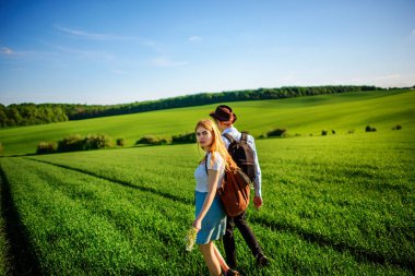 Bir sırt çantası ile bir adam bir şapka ve uzun saçlı bir kadın yol boyunca gidin. Çayır boyunca birkaç yürür.