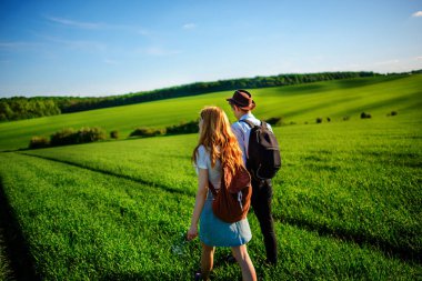 Bir sırt çantası ile bir adam bir şapka ve uzun saçlı bir kadın yol boyunca gidin. Çayır boyunca birkaç yürür.