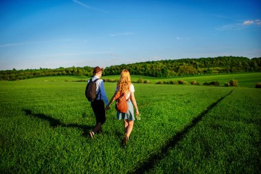 Bir sırt çantası ile bir adam bir şapka ve uzun saçlı bir kadın yol boyunca gidin. Çayır boyunca birkaç yürür.