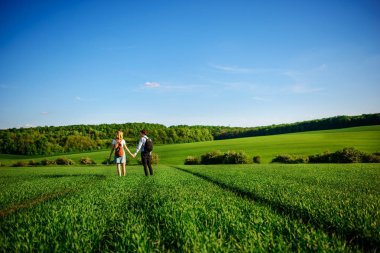 Bir sırt çantası ile bir adam bir şapka ve uzun saçlı bir kadın yol boyunca gidin. Çayır boyunca birkaç yürür.