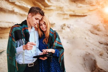 Güzel kadın ve yakışıklı bir battaniyeye sarılmış. Onlar gülümseyen ve bir tablet ekranında bir kum ocağı arka plan üzerinde seyir.