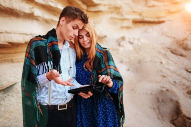 Güzel kadın ve yakışıklı bir battaniyeye sarılmış. Onlar gülümseyen ve bir tablet ekranında bir kum ocağı arka plan üzerinde seyir.