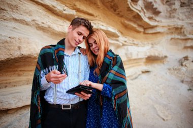 Güzel kadın ve yakışıklı bir battaniyeye sarılmış. Onlar gülümseyen ve bir tablet ekranında bir kum ocağı arka plan üzerinde seyir.