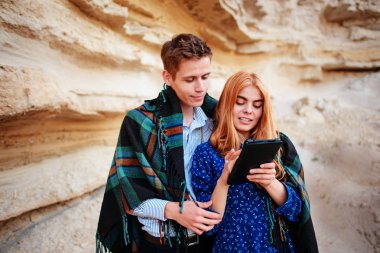 Güzel kadın ve yakışıklı bir battaniyeye sarılmış. Onlar gülümseyen ve bir tablet ekranında bir kum ocağı arka plan üzerinde seyir.