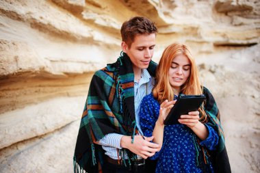 Güzel kadın ve yakışıklı bir battaniyeye sarılmış. Onlar gülümseyen ve bir tablet ekranında bir kum ocağı arka plan üzerinde seyir.