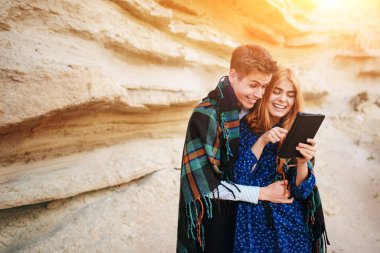 Güzel kadın ve yakışıklı bir battaniyeye sarılmış. Onlar gülümseyen ve bir tablet ekranında bir kum ocağı arka plan üzerinde seyir.
