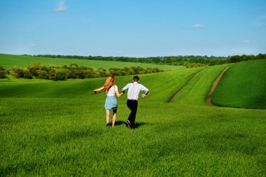 Mutlu aşıklar çayır yeşil çim ve arkasından mavi gökyüzü ile çalışan.