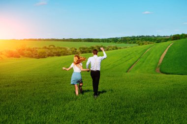 Mutlu aşıklar çayır yeşil çim ve arkasından mavi gökyüzü ile çalışan.