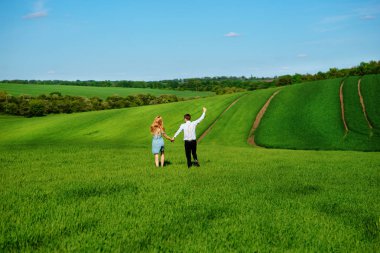Mutlu aşıklar çayır yeşil çim ve arkasından mavi gökyüzü ile çalışan.