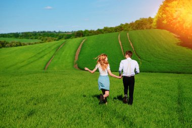 Mutlu aşıklar çayır yeşil çim ve arkasından mavi gökyüzü ile çalışan.