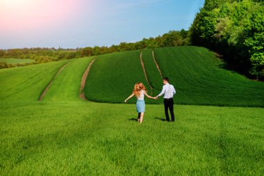 Mutlu aşıklar çayır yeşil çim ve arkasından mavi gökyüzü ile çalışan.