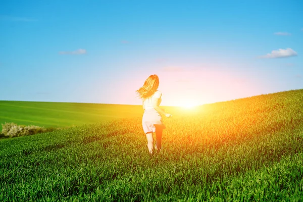 Young beautiful woman running on a green field.