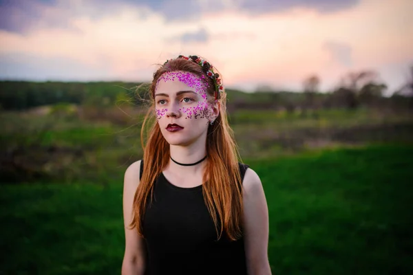 草の上に立って カメラを見て彼女の顔に紫の輝きを持つ若い美しい女性 — ストック写真