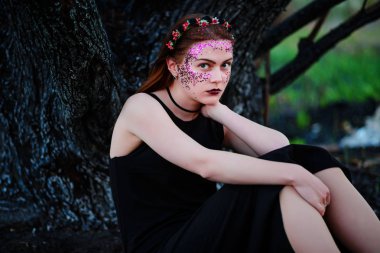 Menekşe Parlatıcı yüzünde güzel bir genç kadınla yanmış bir ağacın yanında duruyor.