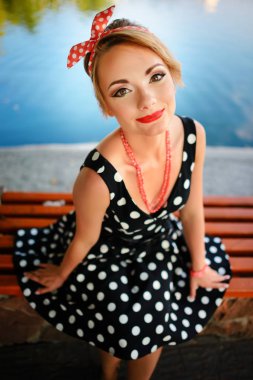 Güzel bir genç kadın giyinmiş gölet yakınındaki bir bankta oturur.