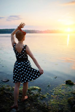 Gün batımını arka plan üzerinde göl kenarında duran giymiş kadın çok güzel genç.