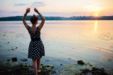 Gün batımını arka plan üzerinde göl kenarında duran giymiş kadın çok güzel genç.