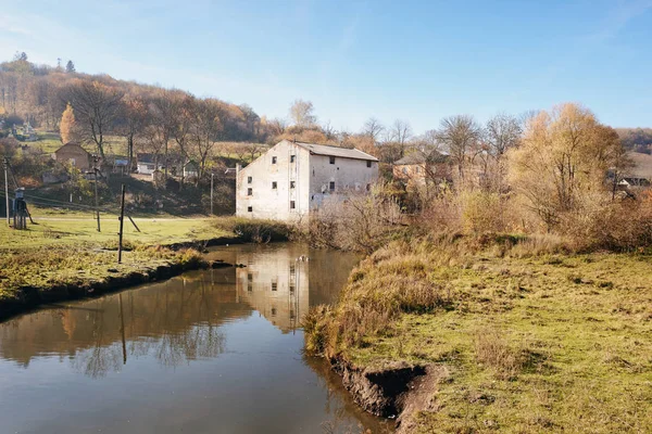 Autumn landscape of the countryside: old non-working watermill near greenfields and flowing river.