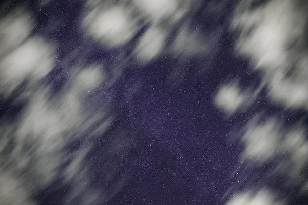 Background of dark-blue night sky with countless twinkle stars and moving white clouds upon on it.