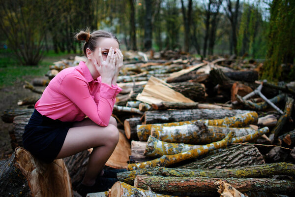 Красивая молодая женщина сидит на стоге срубленных стволов деревьев в лесу
.