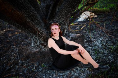 Menekşe Parlatıcı yüzünde güzel bir genç kadınla yanmış bir ağacın yanında duruyor.