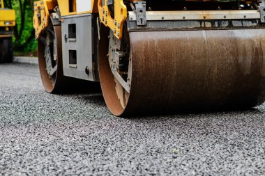 Asfalt silindirinin arka planında sıcak asfalta basın. Yol tamir makinesi.