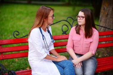 bakan doktor veya Hemşire Genç hastaya açık havada, bir bankta oturan alarak tutun konuşma