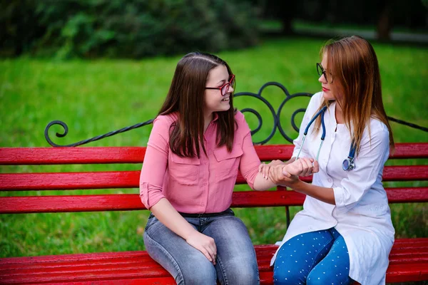 bakan doktor veya Hemşire Genç hastaya açık havada, bir bankta oturan alarak tutun konuşma.