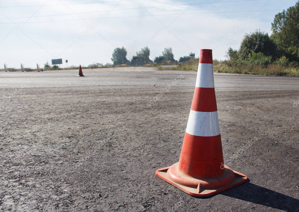 traffic cone, with white and orange stripes on gray asphalt, copy space.