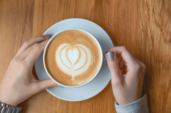 Beautiful heart cafe latte on wooden table with girl hands