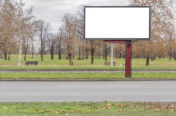 Big red billboard on city road street with asphalt and green lawn with cloudy sky