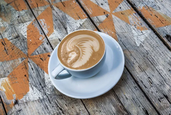 Cup of hot cappuccino with indian head latte art coffee drink on wooden painted table