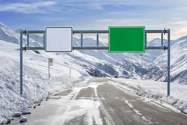 Asphalt road and big road sign with a lot of snow and mountain sky background