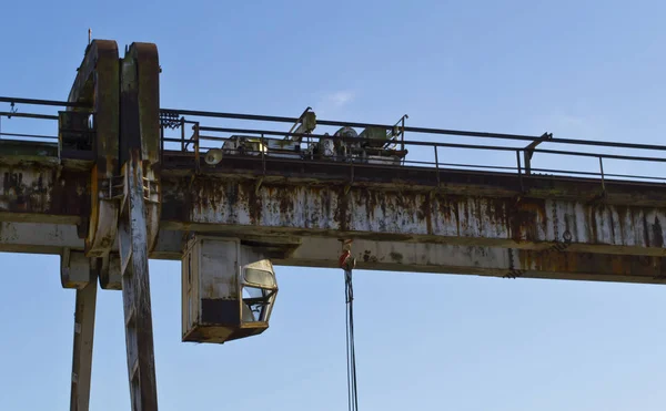 Old, rusty gantry crane with winch and hook over bright blue sky
