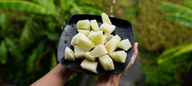 Kesilmiş kavun parçaları, yakın plan siyah bir tabakta bir kızın ellerinde.