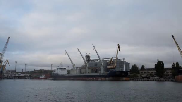 Timelapse of grain terminal at seaport on cloudy day. Cereals bulk transshipment to vessel loading grain crops on bulk ship from large elevators at the berth. Transportation of agricultural products. — Stock Video