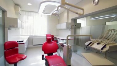 Beyaz diş hekimi ofisi. Lüks minimalist diş kliniği iç cam duvarlar üzerinde diş lamba kırmızı sandalye ve araçları. Ameliyat odası modern donatımın tam çalışma diş hekimliği. Yavaş yavaş hareketli kamera