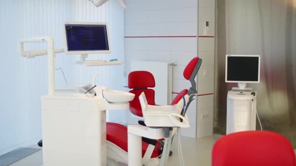 Oficina del dentista blanco. Interior de la clínica dental minimalista de lujo con silla roja y herramientas, lámpara dental sobre paredes de vidrio. Sala de cirugía de odontología llena de equipos modernos. Cámara moviéndose lentamente — Vídeos de Stock