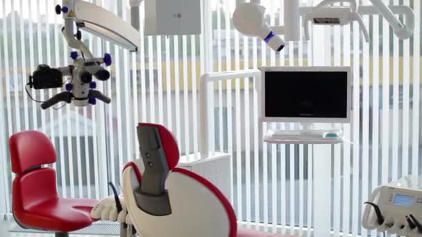 White dentist office. Luxury minimalistic dental clinic interior with red chair and tools, dental lamp over glass walls. Dentistry operating surgery room full of modern equipment. Camera slowly moving — Stock Video