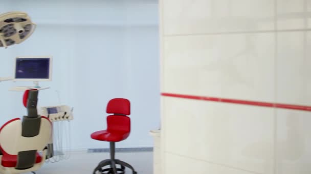 Het kantoor van de wit tandarts. Luxe minimalistische tandheelkundige kliniek interieur met rode stoel en hulpmiddelen, tandheelkundige lamp over glazen wanden. Tandheelkunde operationele operatie kamer vol met moderne apparatuur. Camera langzaam beweegt — Stockvideo