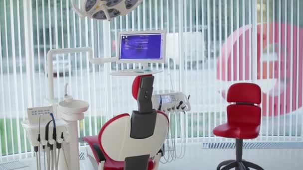 Офис белого дантиста. Роскошный минималистичный интерьер стоматологической клиники с красным креслом и инструментами, стоматологическая лампа над стеклянными стенами. Стоматологическая операционная, полная современного оборудования. Камера медленно движется — стоковое видео