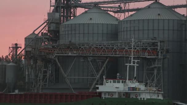Панорама крупного зернового терминала в морском порту вечером. Навальная перевалка зерна на судно ночью. Погрузка зерновых культур на корабль с больших лифтов на причале. Транспорт сельскохозяйственной продукции . — стоковое видео